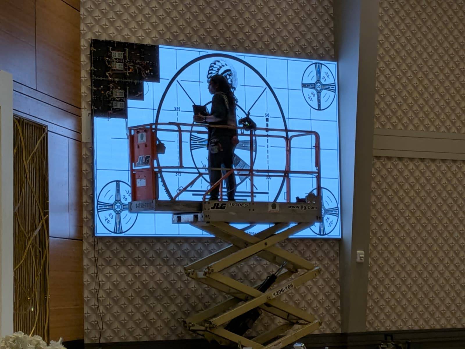 Technician calibrating an LED wall displaying a test pattern from a scissor lift