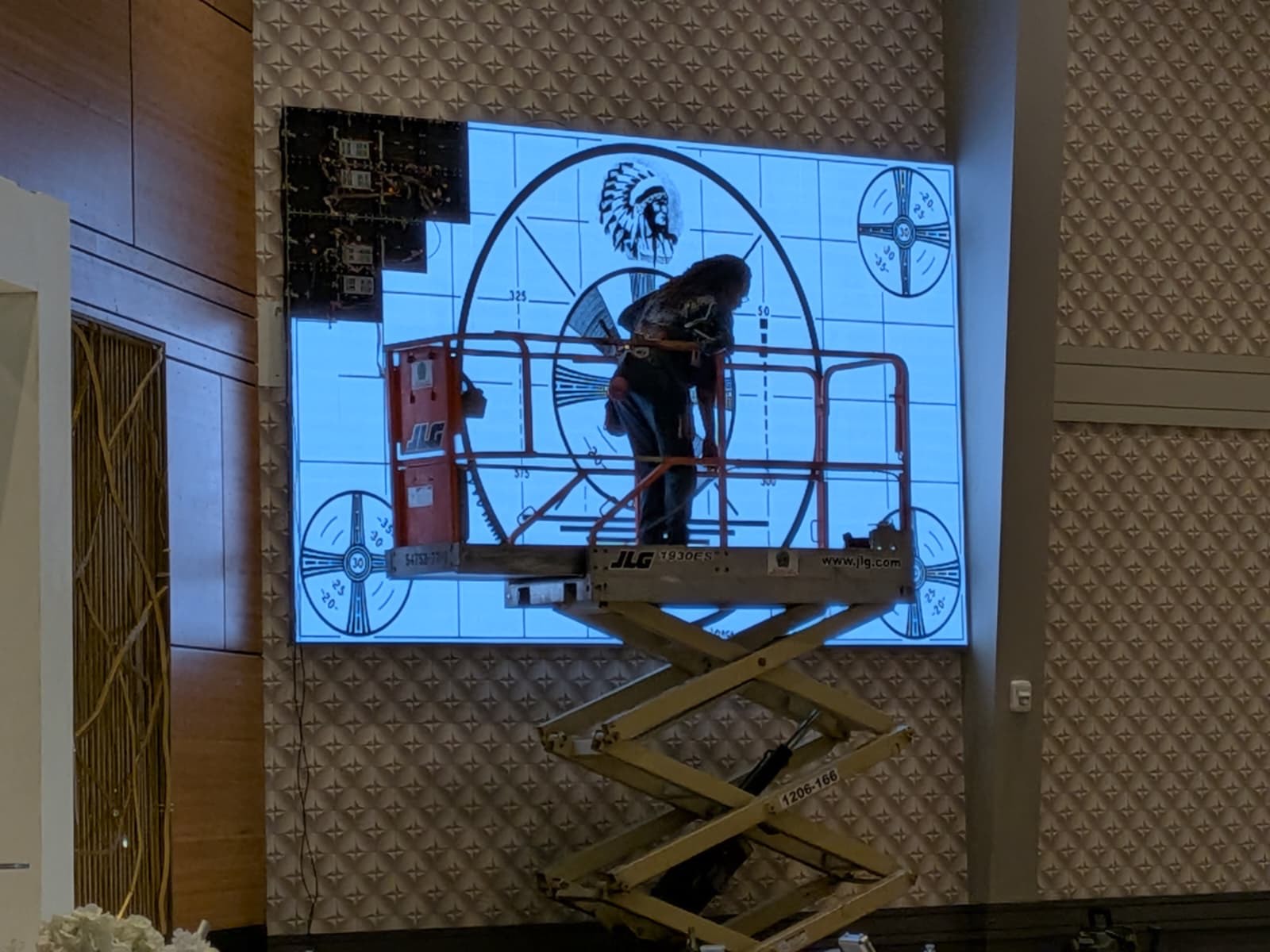 Technician on a scissor lift calibrating an LED wall showing a test pattern