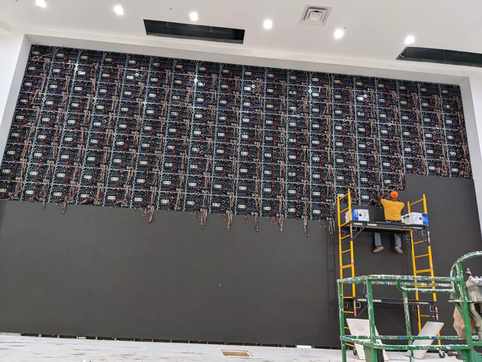 Large LED wall mid-installation with technician placing panels from a scaffold