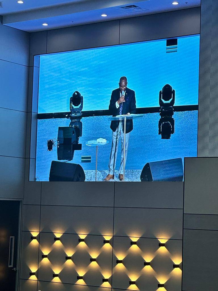 Side LED screen showing live camera feed of a pastor speaking