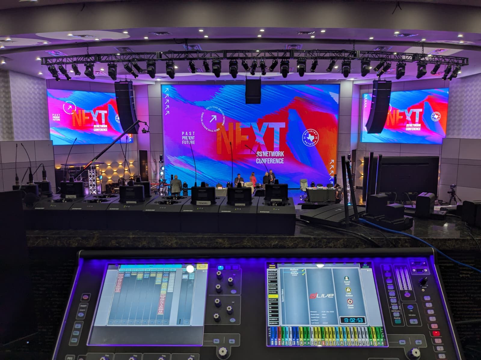 Conference triple LED wall setup with stage lighting, seen from behind the audio mixing console